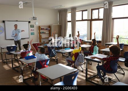 Groupe d'élèves divers levant la main dans la classe à l'école élémentaire Banque D'Images