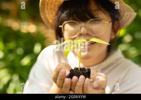 Fille asiatique souriante portant des lunettes et un chapeau de paille, tenant l'usine dans le jardin Banque D'Images