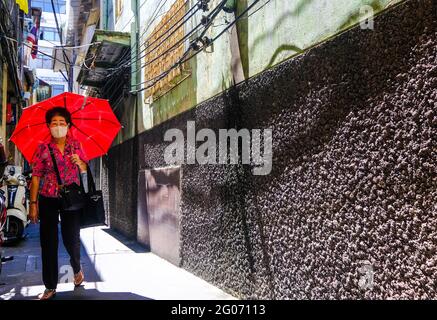 Une femme tenant un parapluie rouge marche le long d'une allée ensoleillée à Chinatown, Bangkok, Thaïlande Banque D'Images