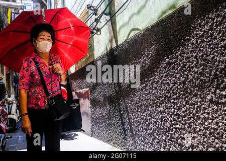 Une femme tenant un parapluie rouge marche le long d'une allée ensoleillée à Chinatown, Bangkok, Thaïlande Banque D'Images