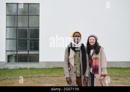Portrait d'un jeune couple multiethnique souriant à l'appareil photo tout en se tenant debout à l'extérieur Banque D'Images