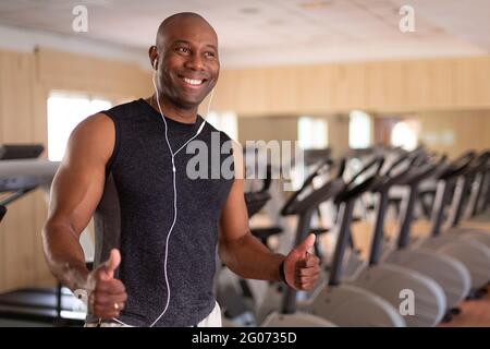 Portrait d'un homme afro-américain souriant dans la salle de gym. Il a les pouces dans l'attitude positive. Concept de sport et de vie saine. Banque D'Images