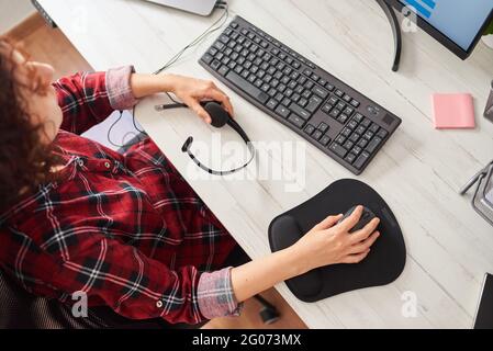 Vue de dessus des mains d'une femme en utilisant la souris de l'ordinateur et en tenant un casque Banque D'Images