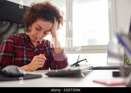 Une femme fatiguée de travailler devant l'ordinateur repose sa tête sur sa main Banque D'Images