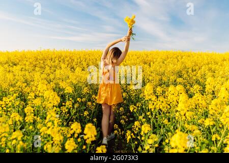 Belle femme avec bouquet posant dans le champ de colza en fleurs avec lumière du coucher du soleil. Banque D'Images