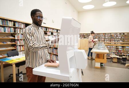 Jeune africain debout dans la bibliothèque et choisissant des livres pour la lecture Banque D'Images