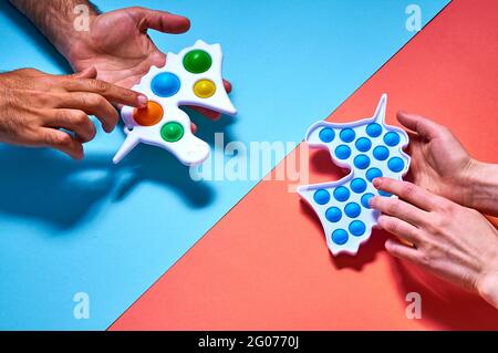 Les mains de femme et d'homme atteignent les jouets à fossettes colorés et tendance sur fond bleu. Banque D'Images