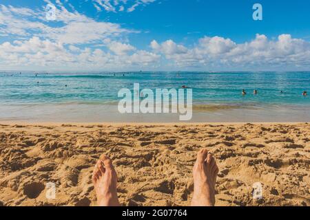 Vue sur les pieds de l'homme sur la plage de sable surplombant l'horizon de l'océan Banque D'Images