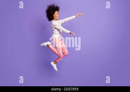 Pleine taille profil photo latérale de afro american petite fille saut ouvert mains copyspace isolé sur fond violet couleur Banque D'Images