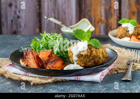 Hamburger à l'agneau, à la carotte, au couscous et à la menthe avec des quartiers épicés de patates douces et de la laitue roquette Banque D'Images