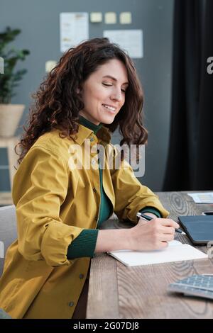 Jeune femme d'affaires assise à la table et écrivant des documents à la table Banque D'Images