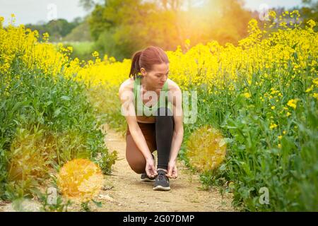 Gros plan de la coureuse qui s'agenouille et noue la cordonneuse à la campagne par temps ensoleillé. Coureur de fond. Banque D'Images