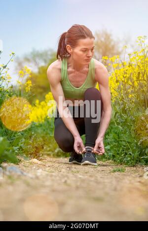 Gros plan de la coureuse qui s'agenouille et noue la cordonneuse à la campagne par temps ensoleillé. Coureur de fond. Banque D'Images