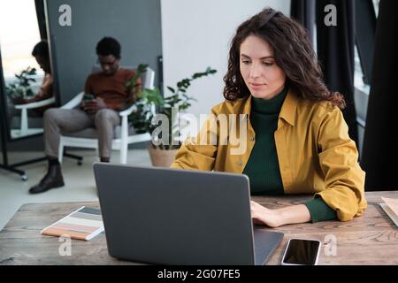 Jeune femme d'affaires assise à la table et travaillant sur un ordinateur portable avec un homme assis à l'arrière-plan au bureau Banque D'Images