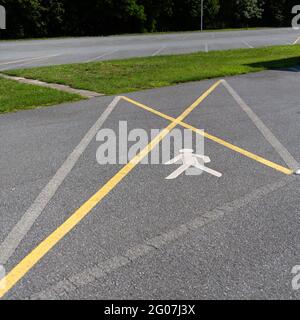 Une croix jaune sur l'asphalte indique que le stationnement est interdit et le symbole piéton indique la marche. Banque D'Images