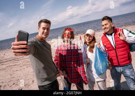 un jeune homme heureux prend le selfie avec des amis tout en ramassant les déchets Banque D'Images