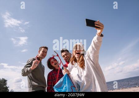 une femme joyeuse prend le selfie avec des amis tout en ramassant les déchets Banque D'Images