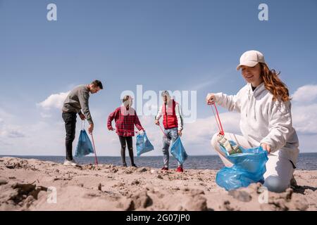 bonne femme tenant un sac poubelle et ramassant des déchets sur le sable près d'un groupe de bénévoles Banque D'Images