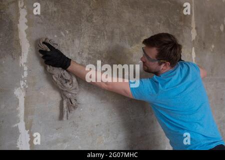 Homme caucasien lavant les murs de la poussière à l'aide d'un vieux chiffon Banque D'Images