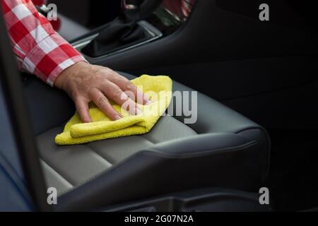 Femme mature nettoyant le siège en cuir de la voiture avec un chiffon doux en microfibre jaune. Banque D'Images