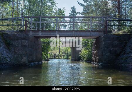 Deux petits ponts modernes - l'un est en bois et l'autre en béton au-dessus d'une crique dans la forêt avec lumière du soleil vive sur les sommets des arbres. Suède, Tavelsjo L. Banque D'Images