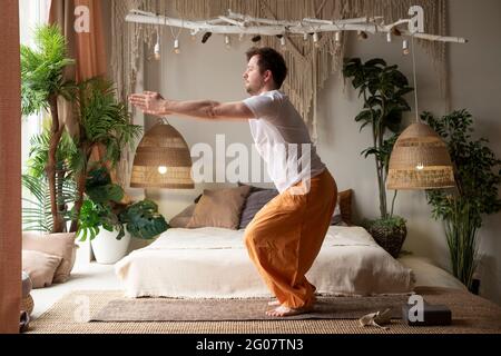 Homme mature en chaise pose ou utkatasana faisant du yoga à la maison Banque D'Images