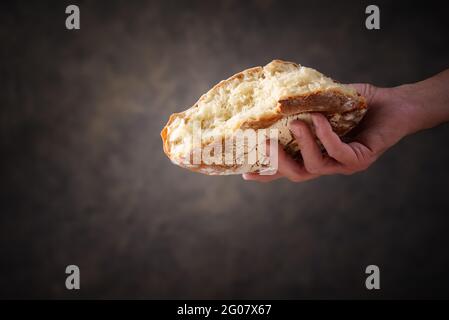 Main donnant un morceau de pain sur fond gris brun foncé. Concept d'aide, geste de l'humanité, gros plan, espace pour le texte. Banque D'Images