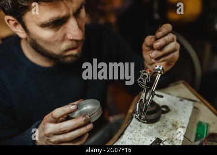 Goldsmith utilisant le chalumeau pour chauffer l'ornement de métal minuscule pendant la fabrication bijoux sur établi Banque D'Images