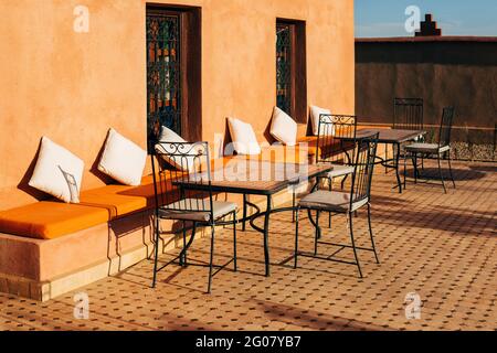 Oreillers moelleux le long d'un mur en pierre avec chaises et tables à Terrasse extérieure confortable de café au Maroc Banque D'Images