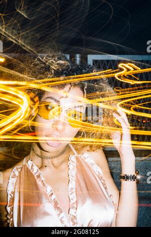 Jeune femme afro-américaine auto-assurée avec des cheveux bouclés dedans des lunettes de soleil tendance et un moment de détente dans la rue le soir feux de gel Banque D'Images