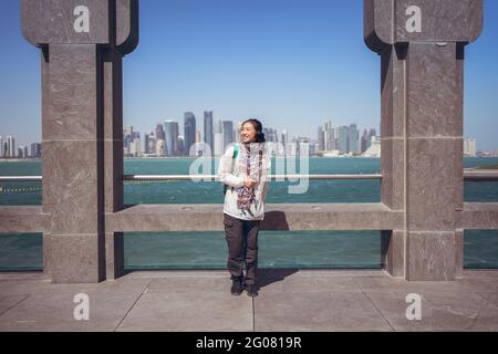 Vue de face d'une joyeuse asiatique touriste souriant à la caméra Tout en se tenant seul à côté de la clôture voûtée sur le front de mer dans le musée De l'art islamique contre nous Banque D'Images