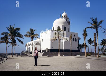 Jeune touriste femelle se tenant sur la place pavée au beau blanc Bâtiment de l'île Mosquée avec ciel bleu clair en arrière-plan En journée ensoleillée à Jedd Banque D'Images