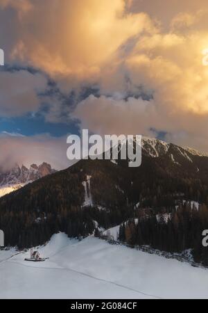 Église de Santa Maddalena avec d'épais nuages flottant sur des sommets de montagnes enneigées dans les Dolomites majestueuses, Italie. Banque D'Images