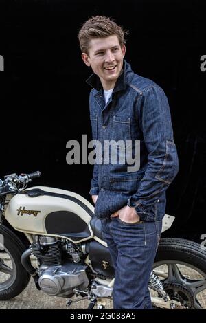 Portrait d'un jeune homme de moto heureux portant un Jean denim avec une moto de café-coureur . Arrière-plan noir. Banque D'Images