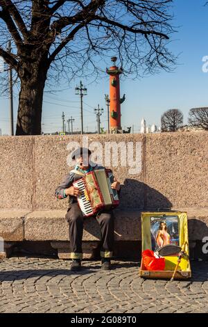 Un musicien de rue joue un accordéon sur la broche de l'île Vasilievsky. En arrière-plan se trouve une colonne Rostral. Russie Saint-Pétersbourg. Banque D'Images