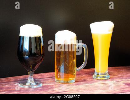 Trois verres avec différentes sortes de bière, sombre, clair et blé, se tiennent dans une rangée sur une table en bois. Gros plan. Banque D'Images