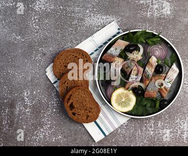 Filet de hareng aux oignons, aux olives et aux herbes sur une assiette ronde sur fond sombre. Vue de dessus, plan d'appartement Banque D'Images