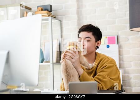 Jeune femme de tomboy asiatique en tenue décontractée tenant son chat pendant le travail de la maison dans la salle de séjour Banque D'Images