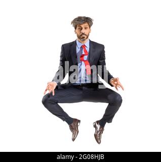 Homme d'affaires à barbe plein d'énergie en costume élégant sautant dans l'air sur blanc dans une vue frontale avec des jambes tordues regardant la caméra Banque D'Images
