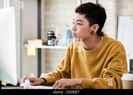 Jeune femme de tomboy asiatique en tenue décontractée travaillant de la maison dans le salon Banque D'Images