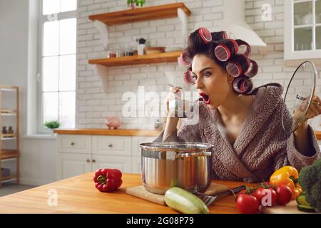 Choqué femme au foyer dans la cuisine dégustation de sa soupe se rendant compte qu'elle est trop salée. Banque D'Images