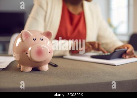 Piggy banque sur la table de près, femme calculant l'épargne ou les bénéfices d'affaires en arrière-plan Banque D'Images