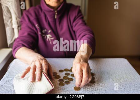 Femme âgée préoccupée assise à la maison et comptant les pièces de monnaie restantes.Old femme assise misérablement à la table à la maison et comptant pièces restantes pour Banque D'Images