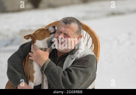 Le joli chien basenji murmure son maître vous aime tout en étant assis sur les mains de l'homme âgé caucasien en hiver Banque D'Images