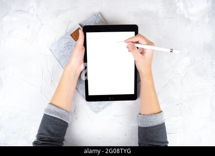 Rognez la vue des mains des femmes à l'aide d'une tablette numérique et d'un crayon à stylet sur un arrière-plan en béton léger. Maquette d'une tablette. Artiste au travail. Banque D'Images