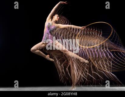 Portrait de la jeune fille rythmique gymnaste en mouvement et en action isolé dans la lumière mélangée sur fond sombre. Banque D'Images