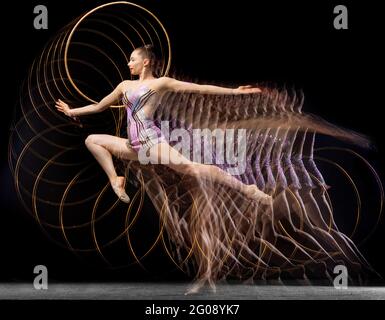 Portrait de la jeune fille rythmique gymnaste en mouvement et en action isolé dans la lumière mélangée sur fond sombre. Banque D'Images