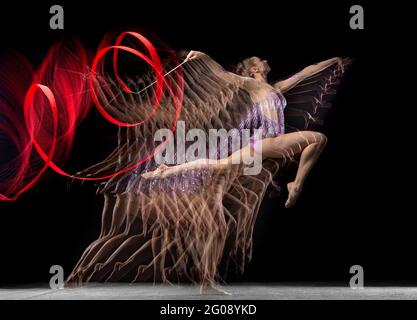 Jeune fille gracieuse gymnast rythmique en mouvement isolé dans la lumière mixte sur fond sombre. Banque D'Images