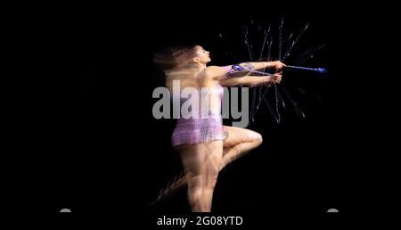 Portrait de la jeune fille rythmique gymnaste en mouvement et en action isolé dans la lumière mélangée sur fond sombre. Banque D'Images