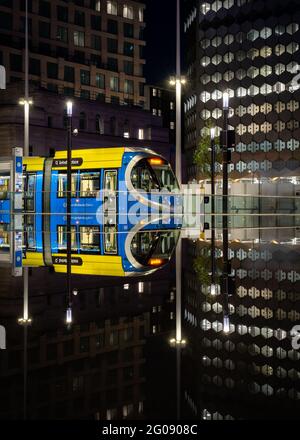 Birmingham Angleterre moderne ville transports en commun tramway bleu de métro à la place Centenaire se reflète dans l'eau la nuit avec un paysage urbain moderne derrière Banque D'Images
